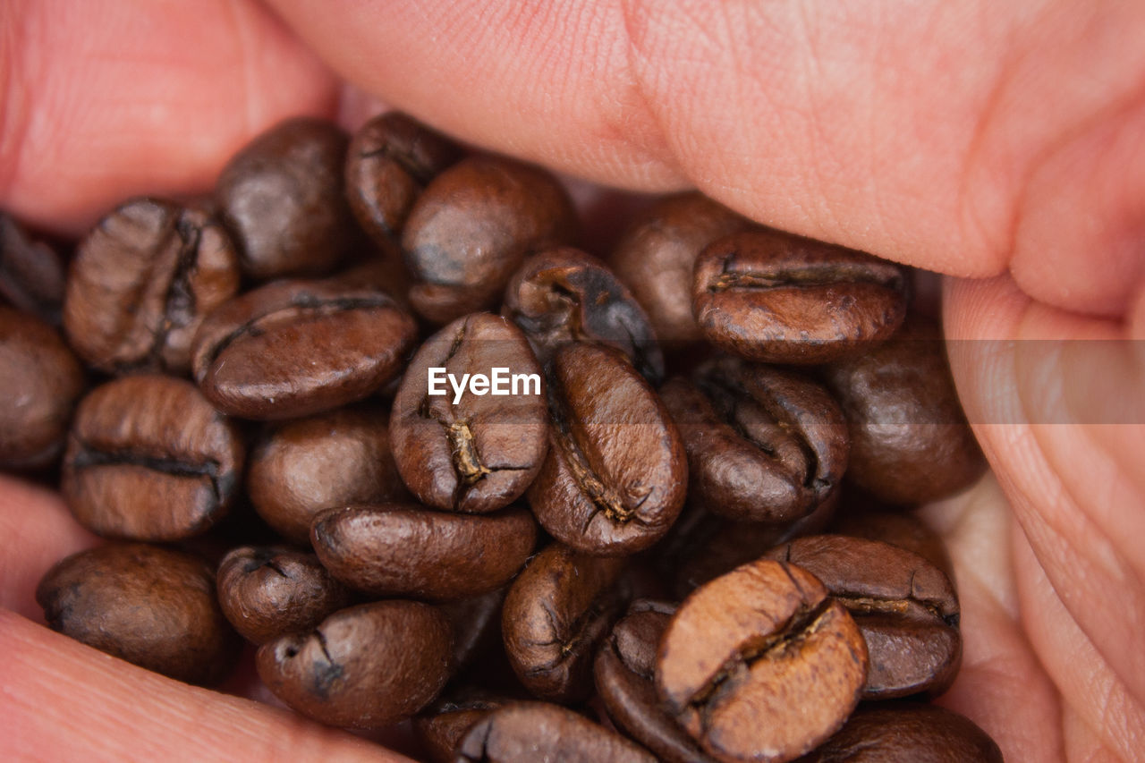 CLOSE-UP OF HAND HOLDING COFFEE BEANS IN THE BACKGROUND