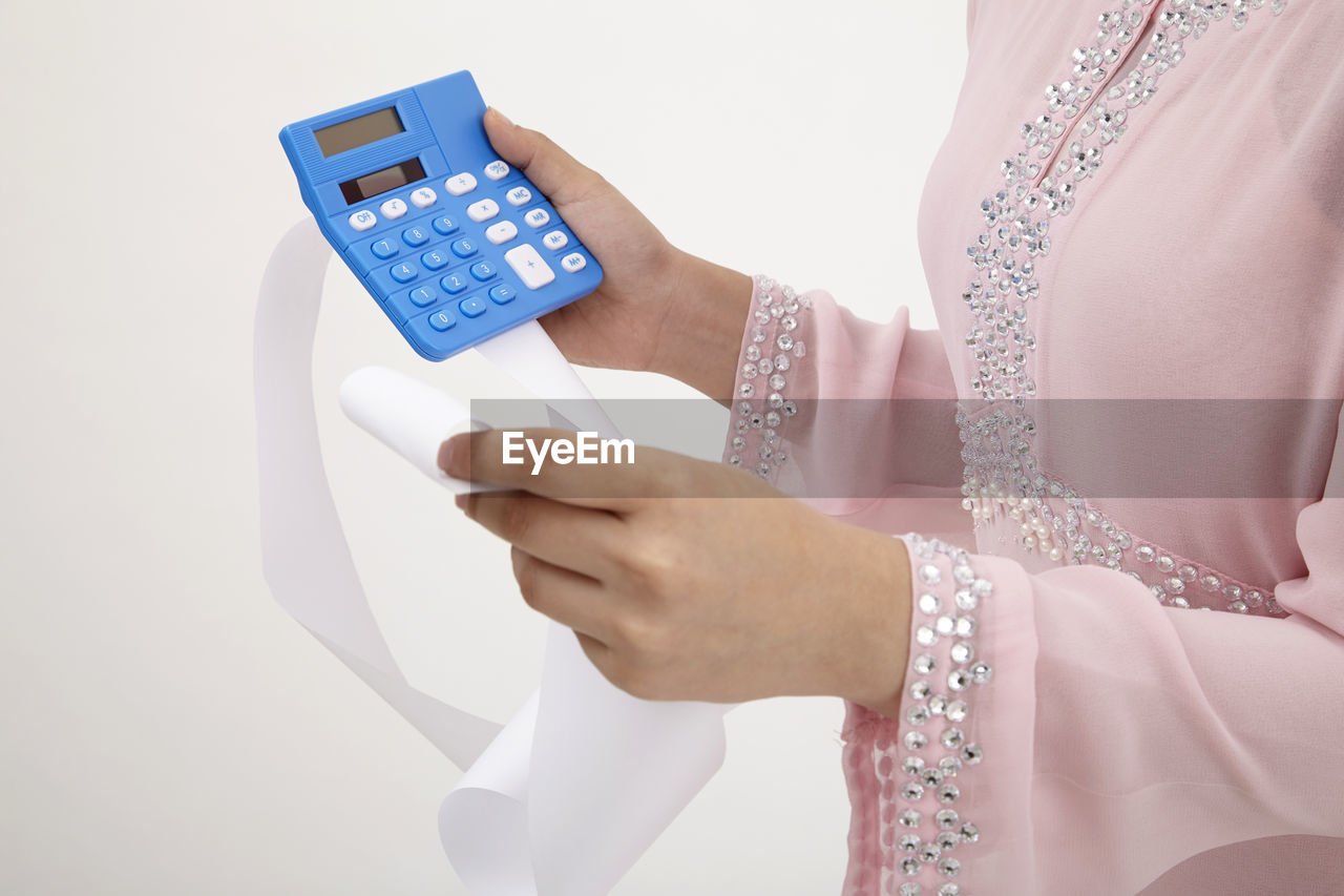 Midsection of woman holding receipt and calculator against white background