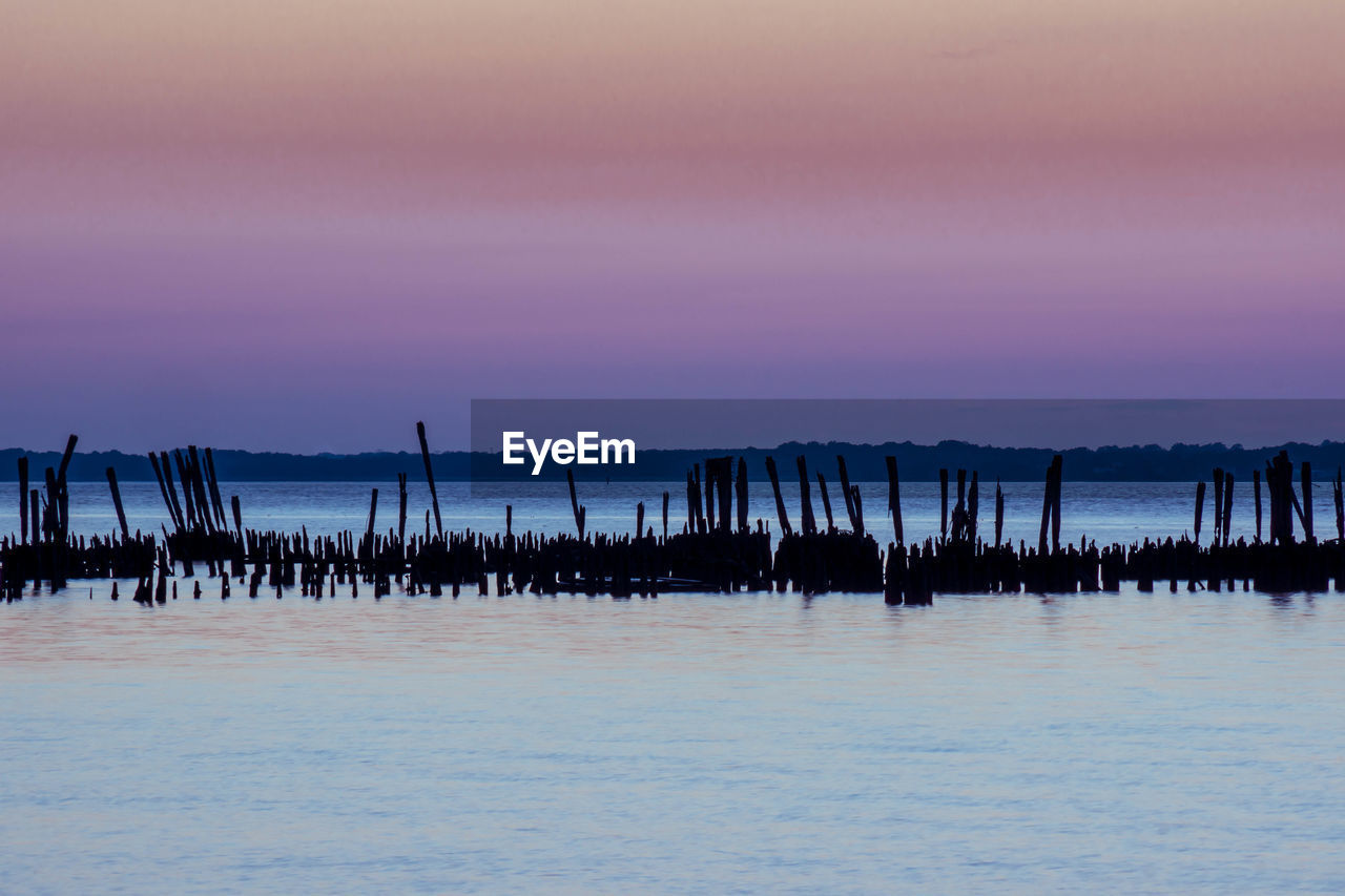 Silhouette wooden post in seascape during sunset