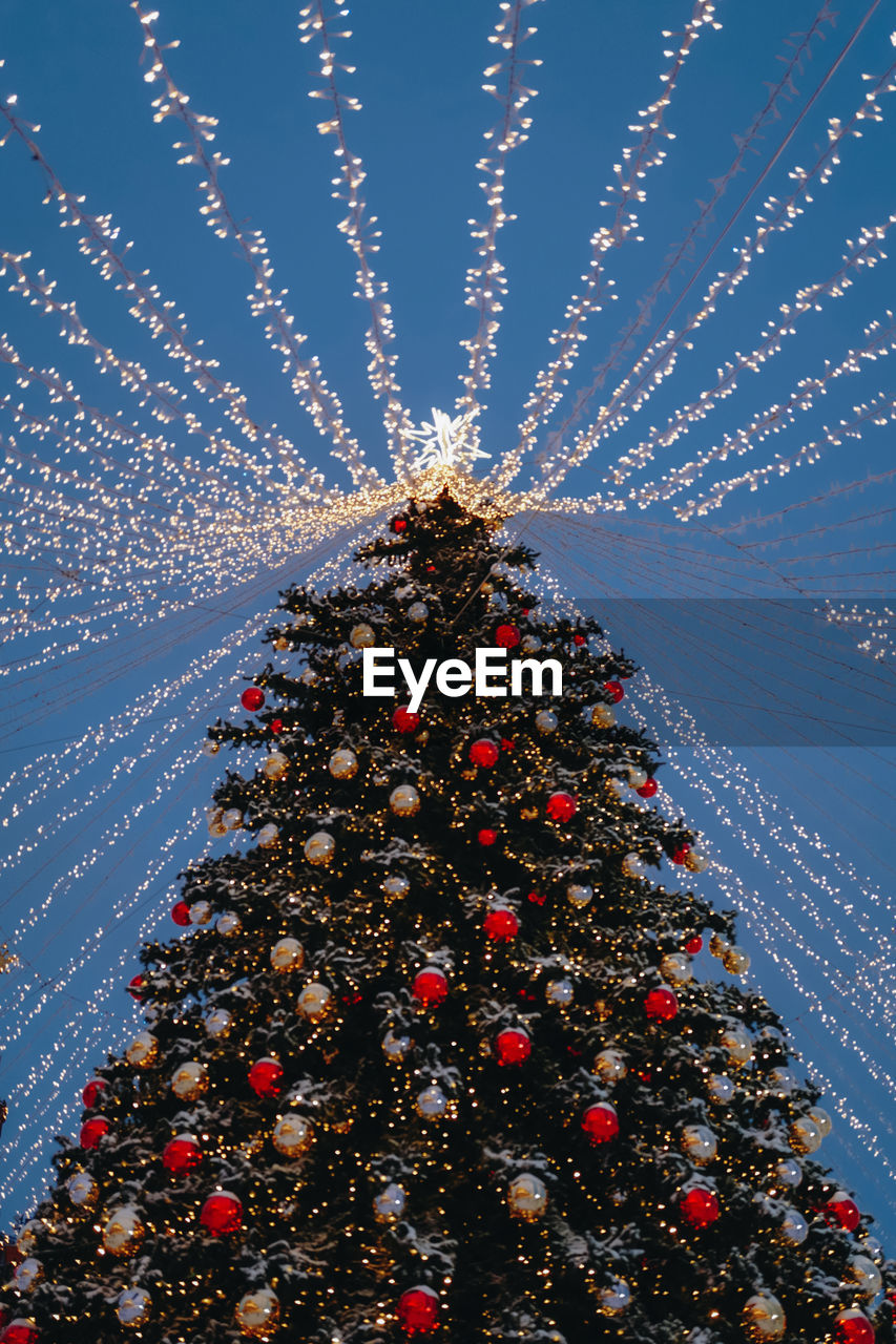 Christmas tree with red toy balls, star and golden lights in the festive evening city bokeh garlands