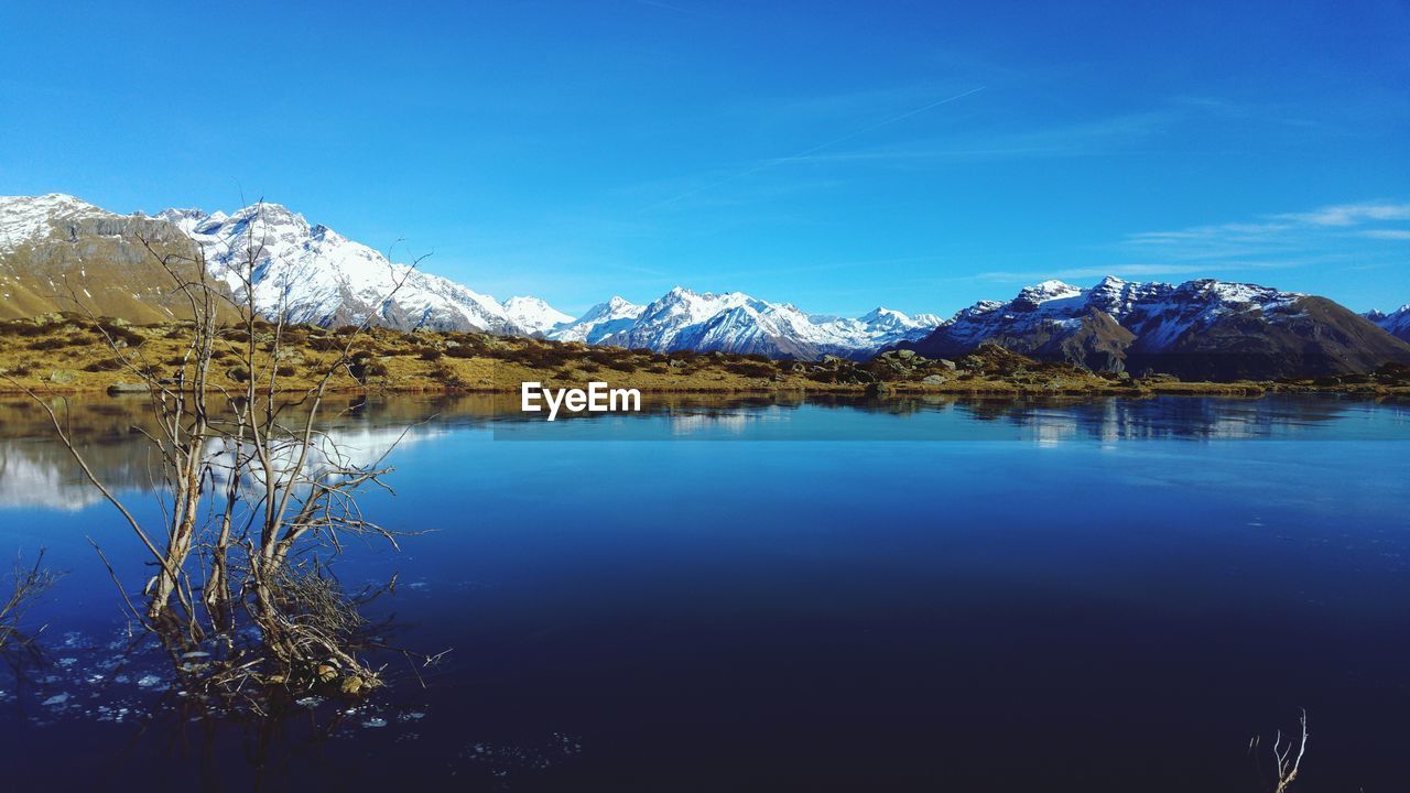Scenic view of lake and snowcapped mountains against blue sky