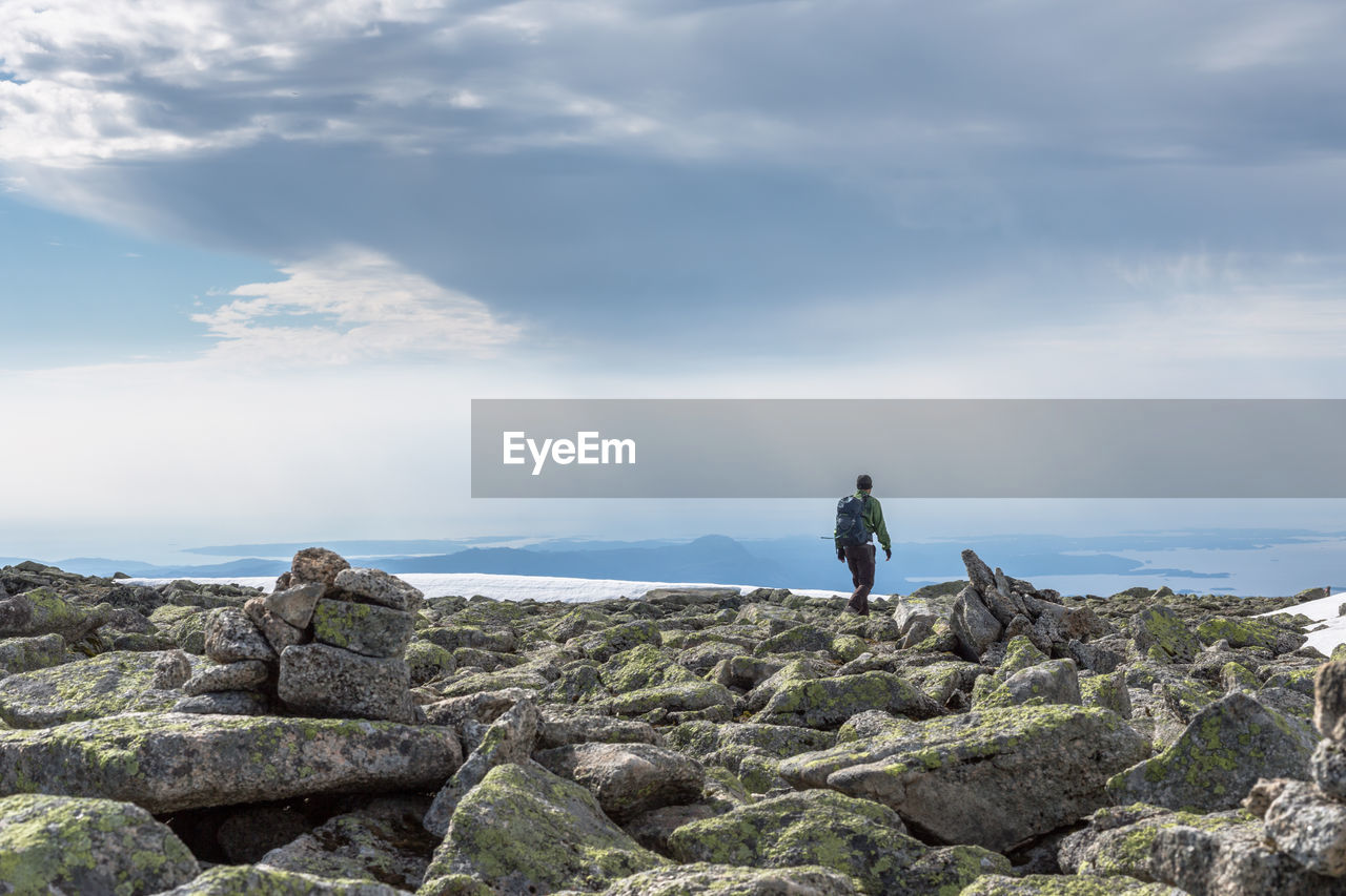 Rear view of hiker on rocks at mountain peak against sky