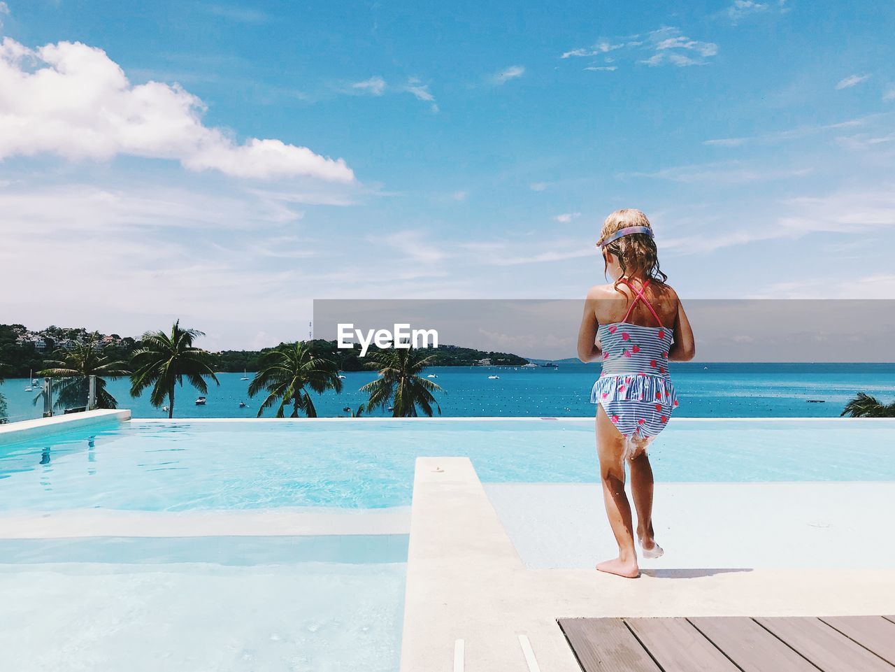 Rear view of girl standing at infinity pool