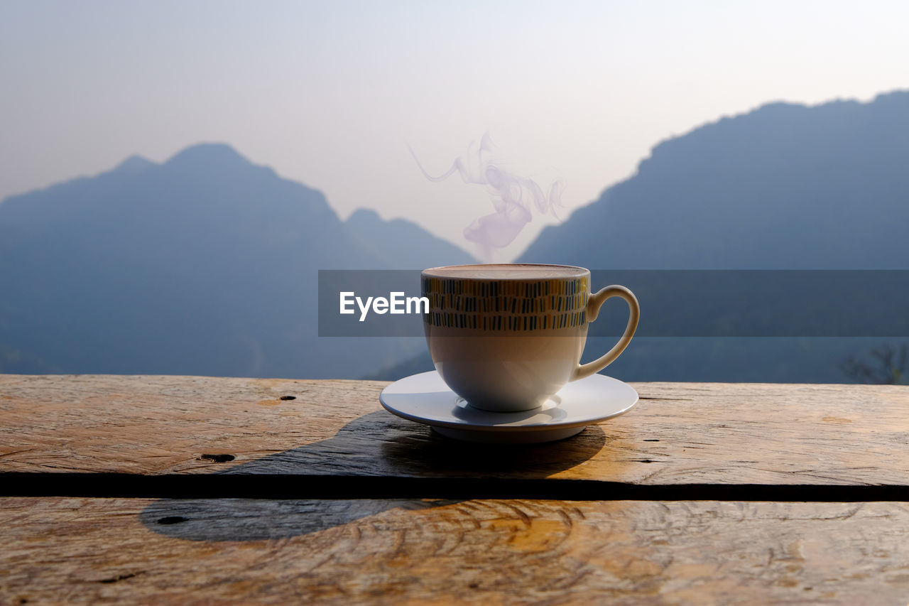 Coffee cup on table against mountains at morning