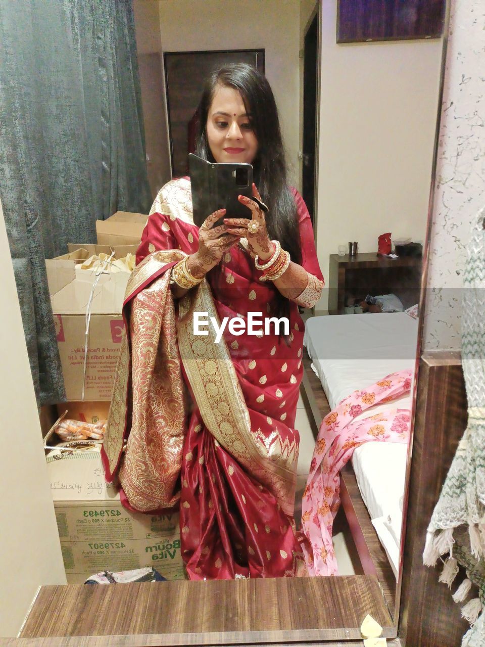 one person, women, adult, clothing, holding, traditional clothing, smiling, front view, female, portrait, communication, indoors, dress, lifestyles, architecture, happiness, sari, looking at camera, young adult, standing, art, wireless technology, emotion, full length, costume, looking, sitting, technology, person