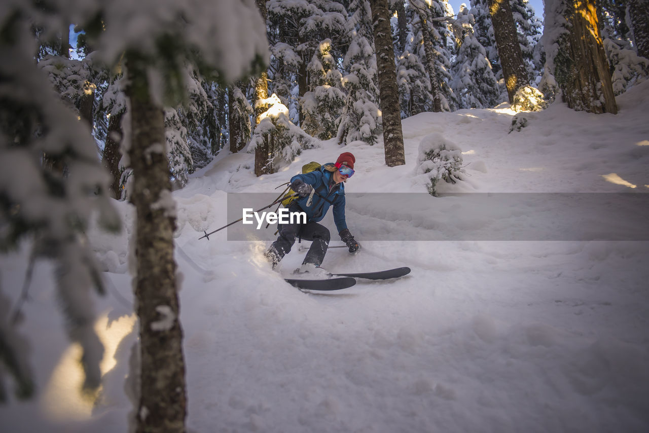 Woman skiing down between trees in red heather, squamish