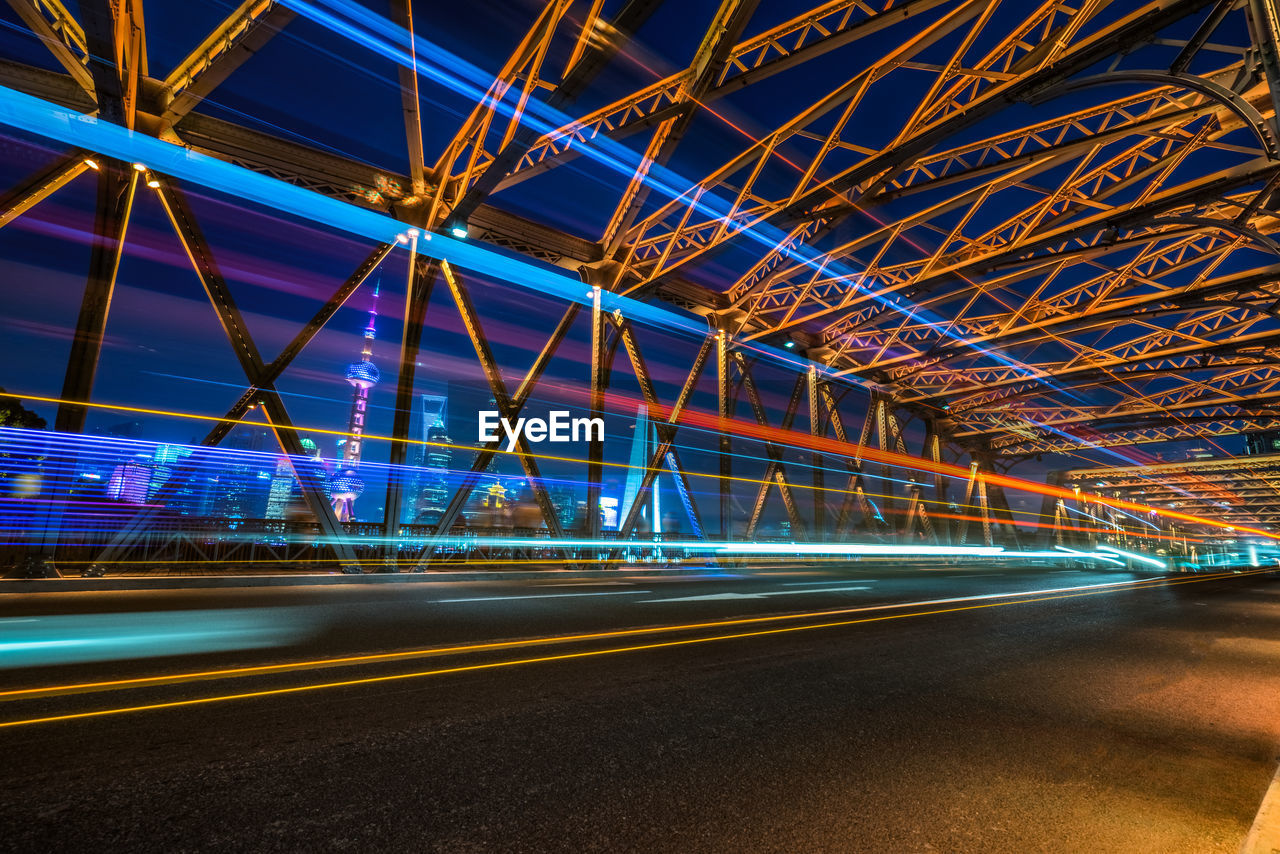 LIGHT TRAILS ON ILLUMINATED BRIDGE AT NIGHT