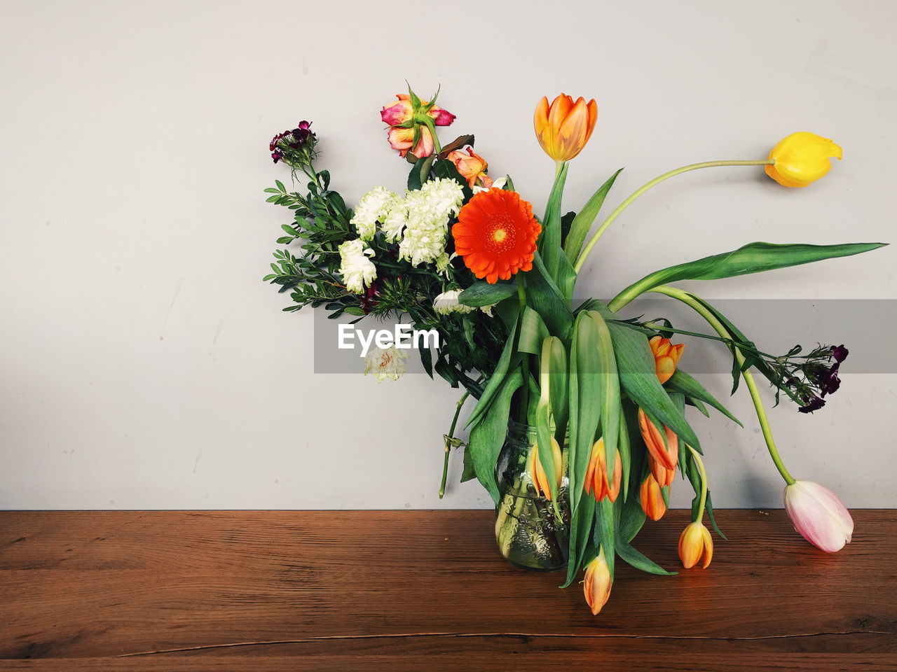 Close-up of flowers in vase on table against wall