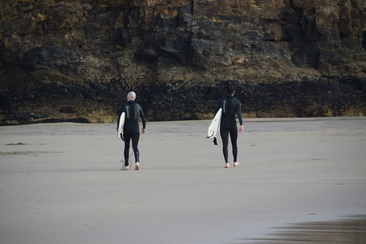 REAR VIEW OF MEN WALKING ON BEACH AGAINST SEA