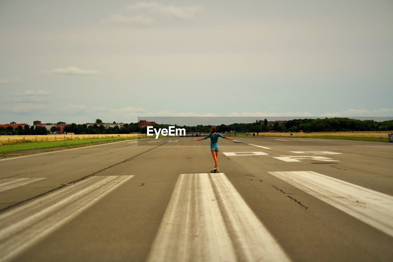 Rear view of woman skateboarding at tempelhof airport runway