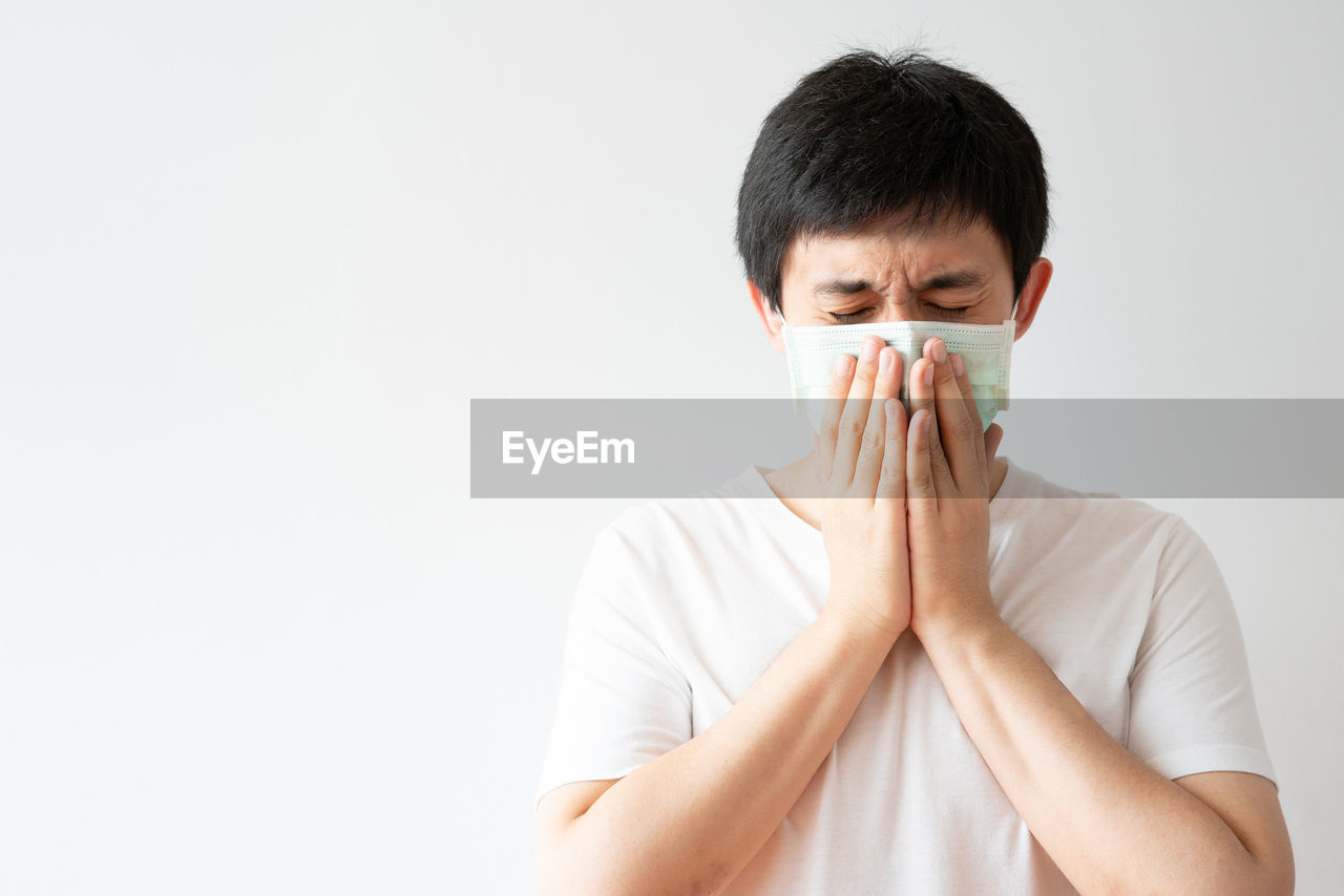 PORTRAIT OF MAN COVERING FACE WITH WHITE BACKGROUND