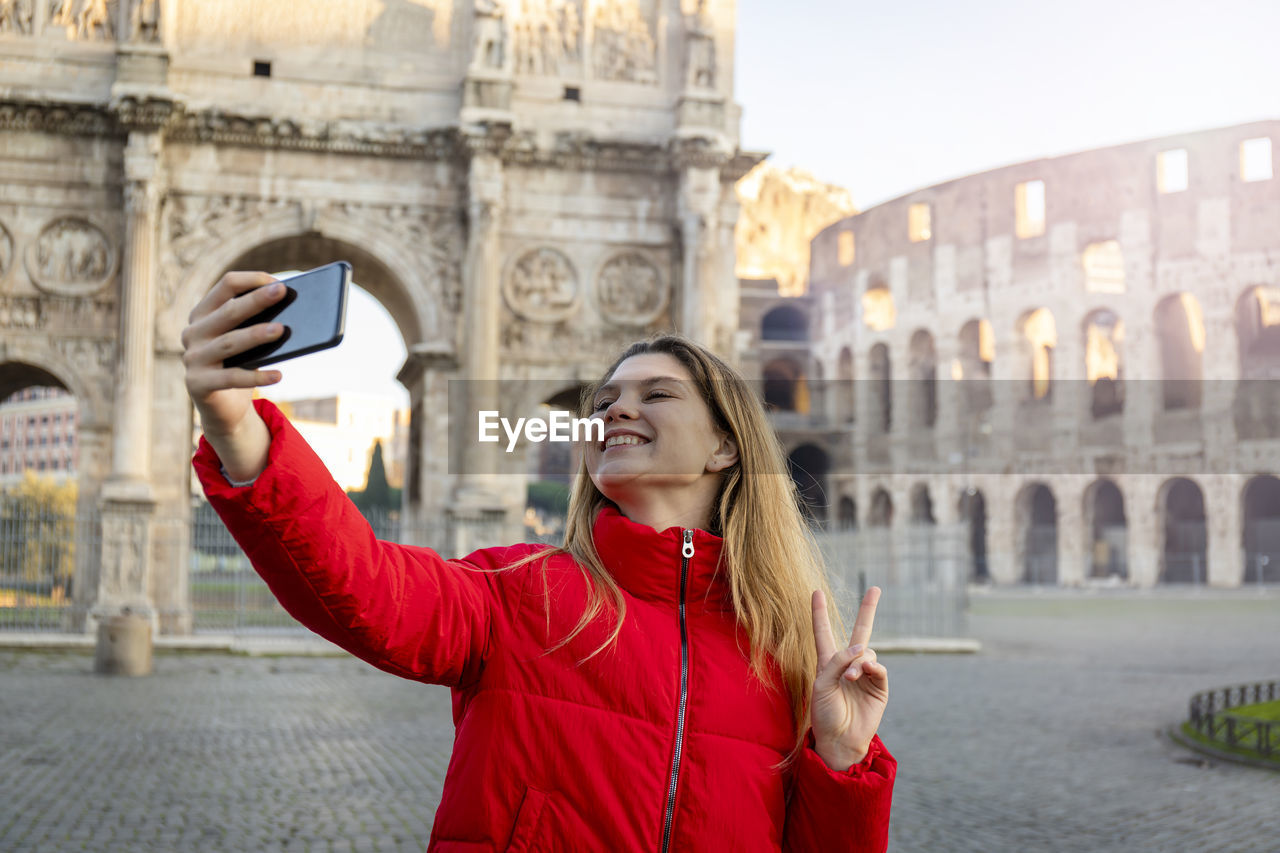 Young charming woman making a selfie in front of the colosseum during a winter vacation. 