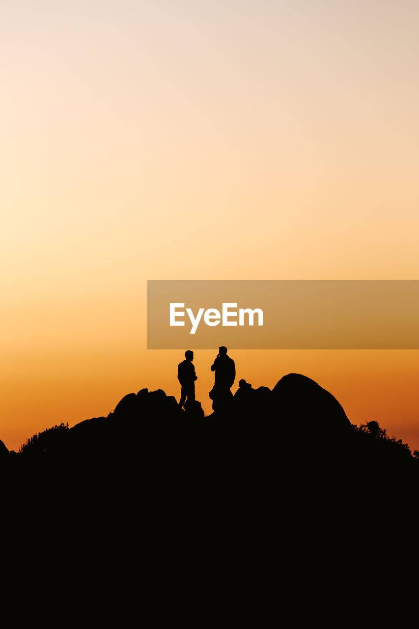 Silhouette people on rock against sky during sunset