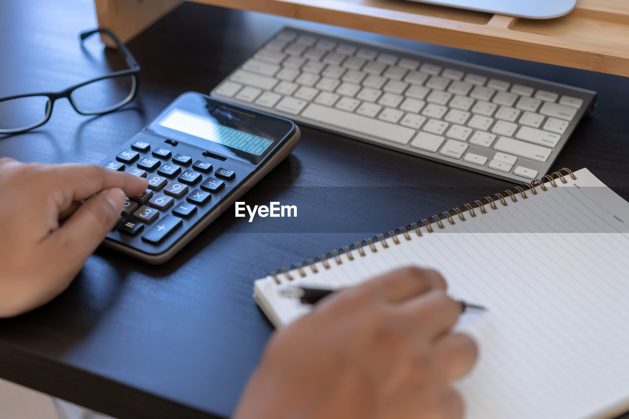 Cropped hands of business person using calculator at desk