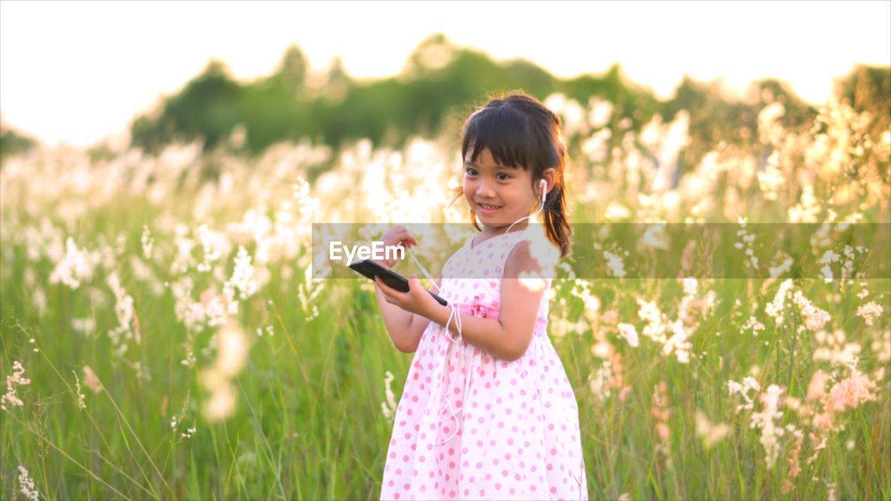Smiling girl listening to music while standing against plants