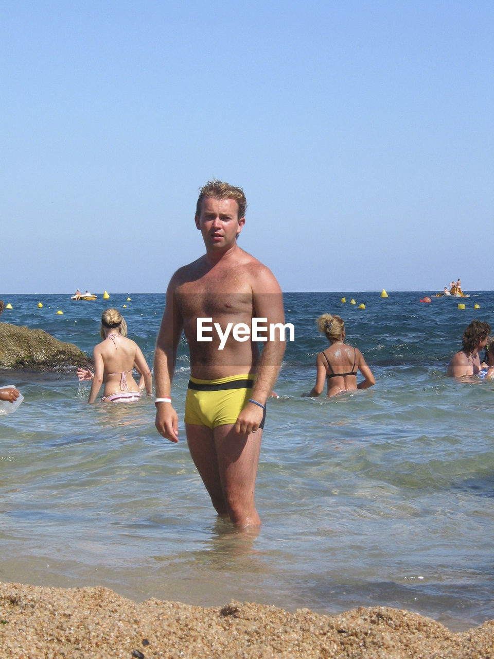 FULL LENGTH OF SHIRTLESS MAN STANDING ON BEACH AGAINST CLEAR SKY