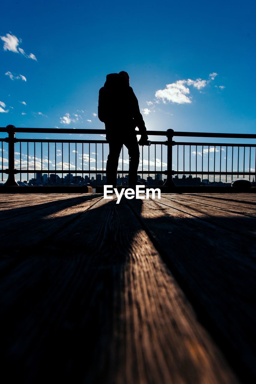 SILHOUETTE MAN STANDING ON FOOTBRIDGE AGAINST SKY