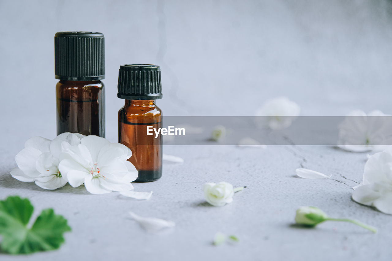 Top view of glass bottles of geranium essential oil with fresh white flowers and petals over gray