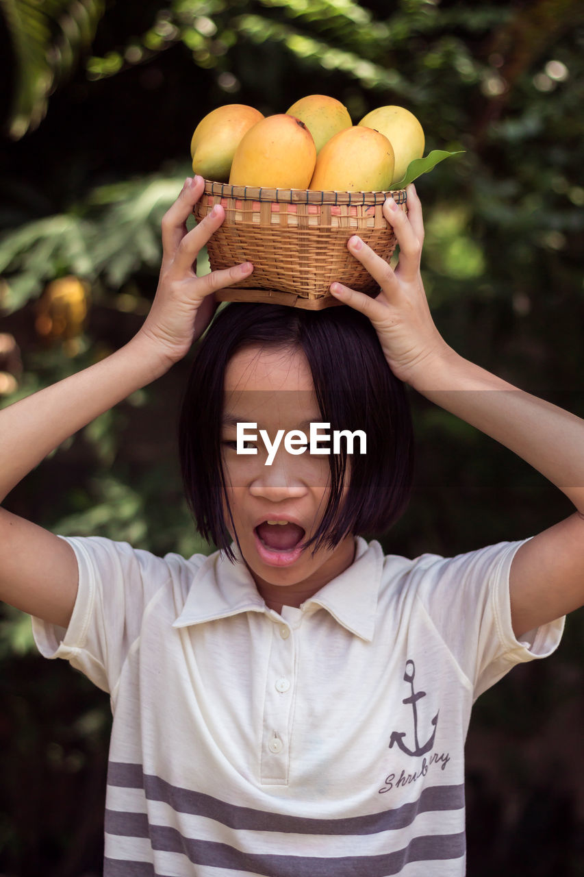 Girl carrying mango fruits with basket on head at farm