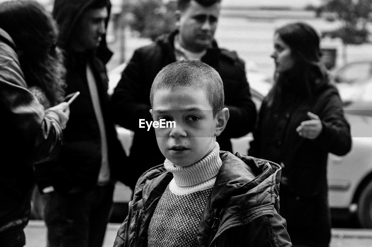 Boy looking away while standing with people in city