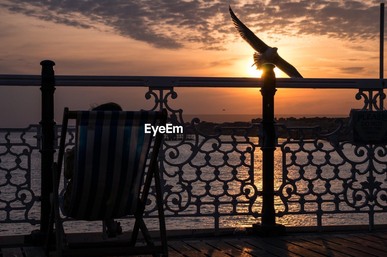 Person sitting on chair at pier against sea during sunset