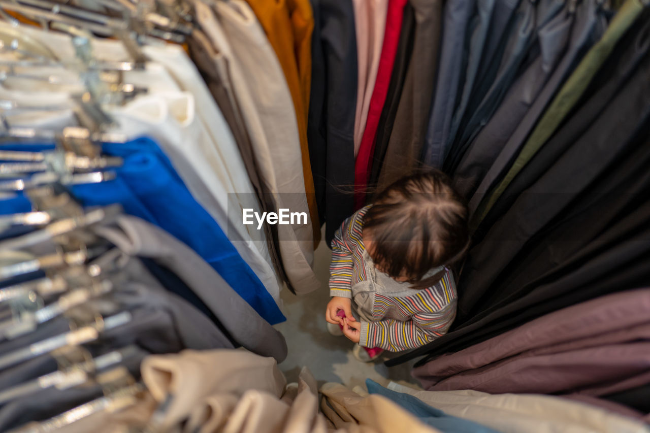 High angle view of girl standing amidst clothes rack