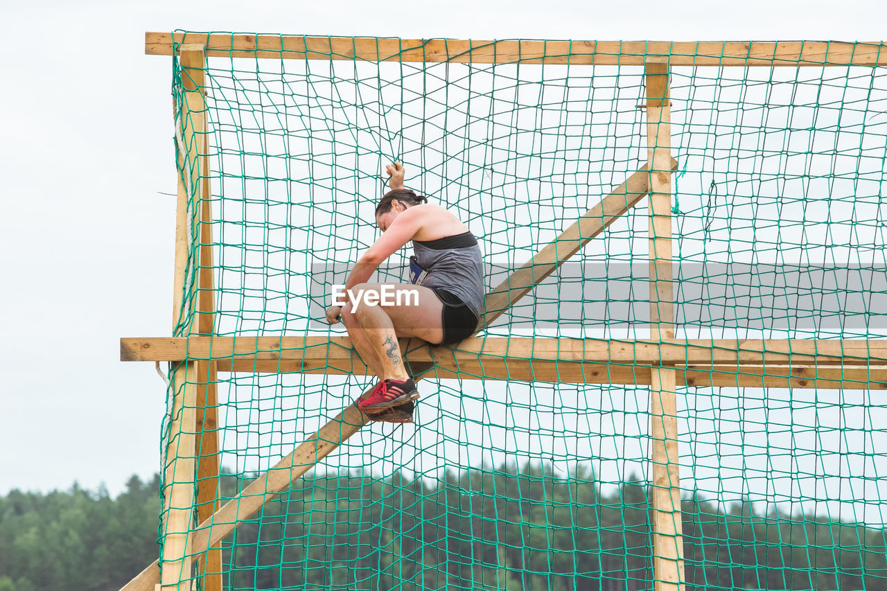 LOW ANGLE VIEW OF MAN CLIMBING ON FENCE