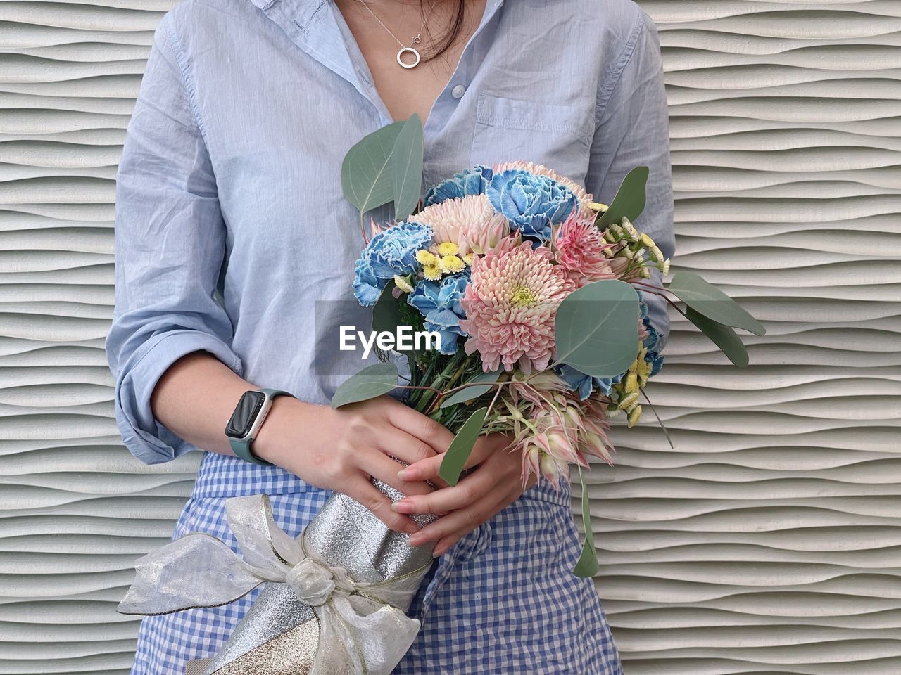 LOW SECTION OF WOMAN HOLDING BOUQUET AGAINST WALL