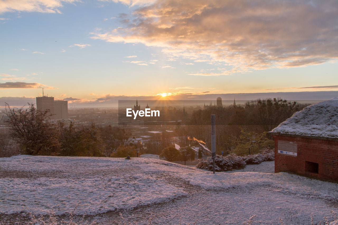 Snow covered cityscape against sky during sunset