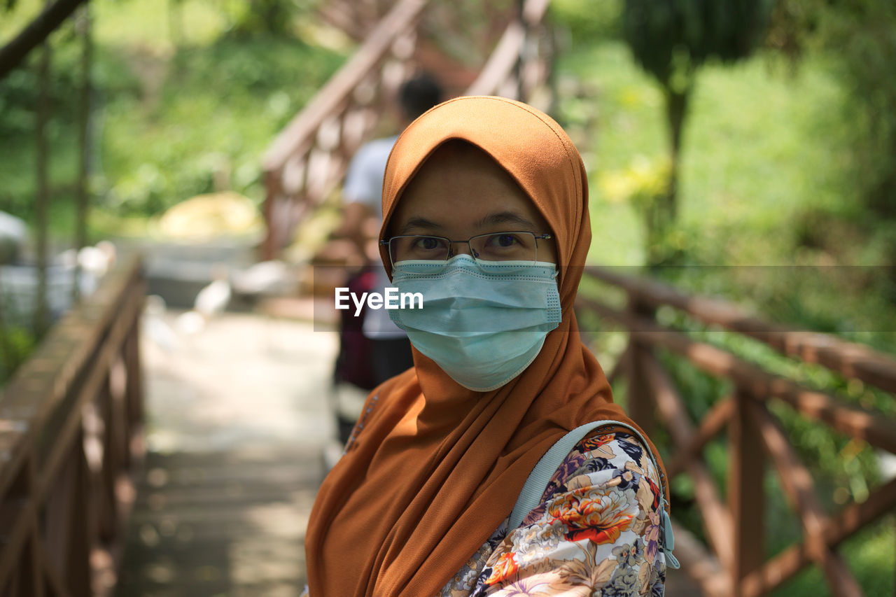 Portrait of woman wearing flu mask standing on footbridge in park