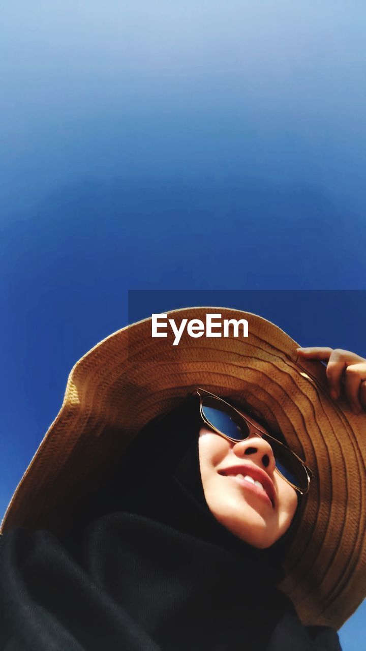 Close-up of woman wearing sunglasses and hat against clear sky