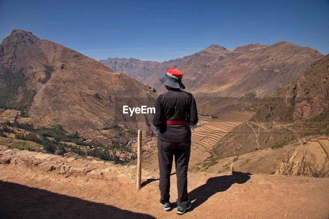 Rear view of woman standing on pisac archaeological site with beautiful view on agricultural field