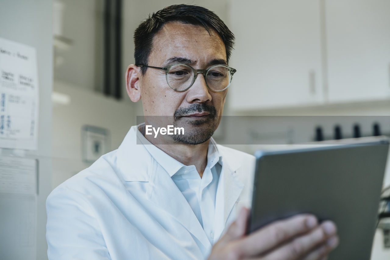 Scientist wearing eyeglasses working on digital tablet while standing at laboratory