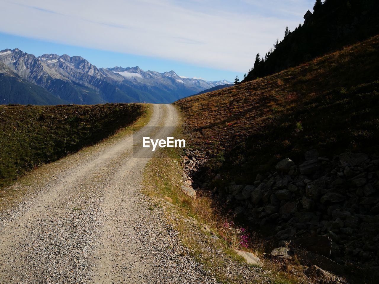 Dirt road by mountains against sky