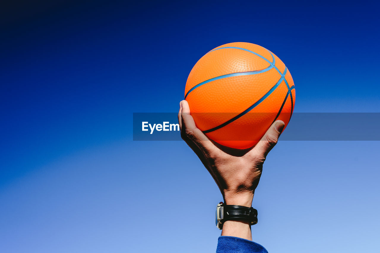 LOW ANGLE VIEW OF MAN PLAYING WITH BALL AGAINST BLUE SKY