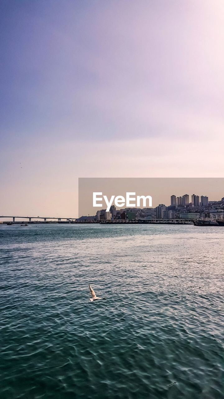 VIEW OF CITY BY SEA AGAINST SKY DURING SUNSET