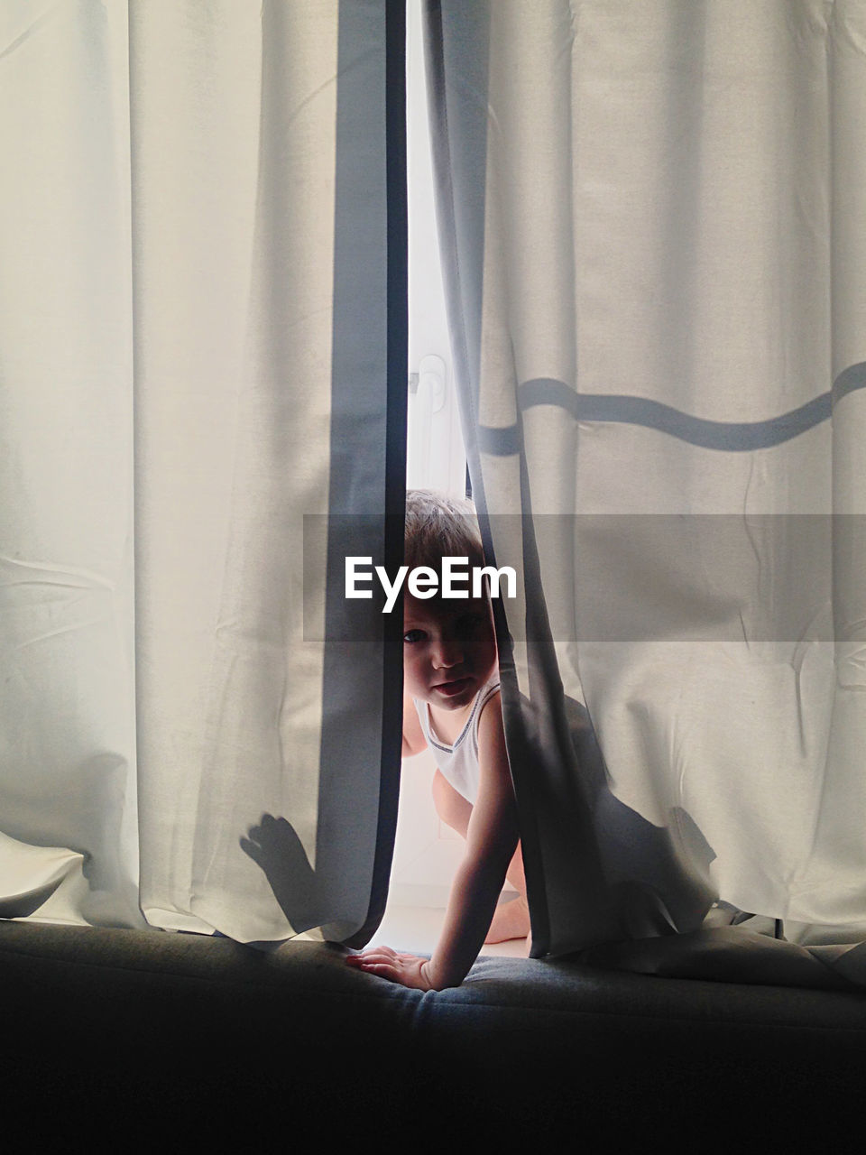 Close-up of boy hiding in curtain at home