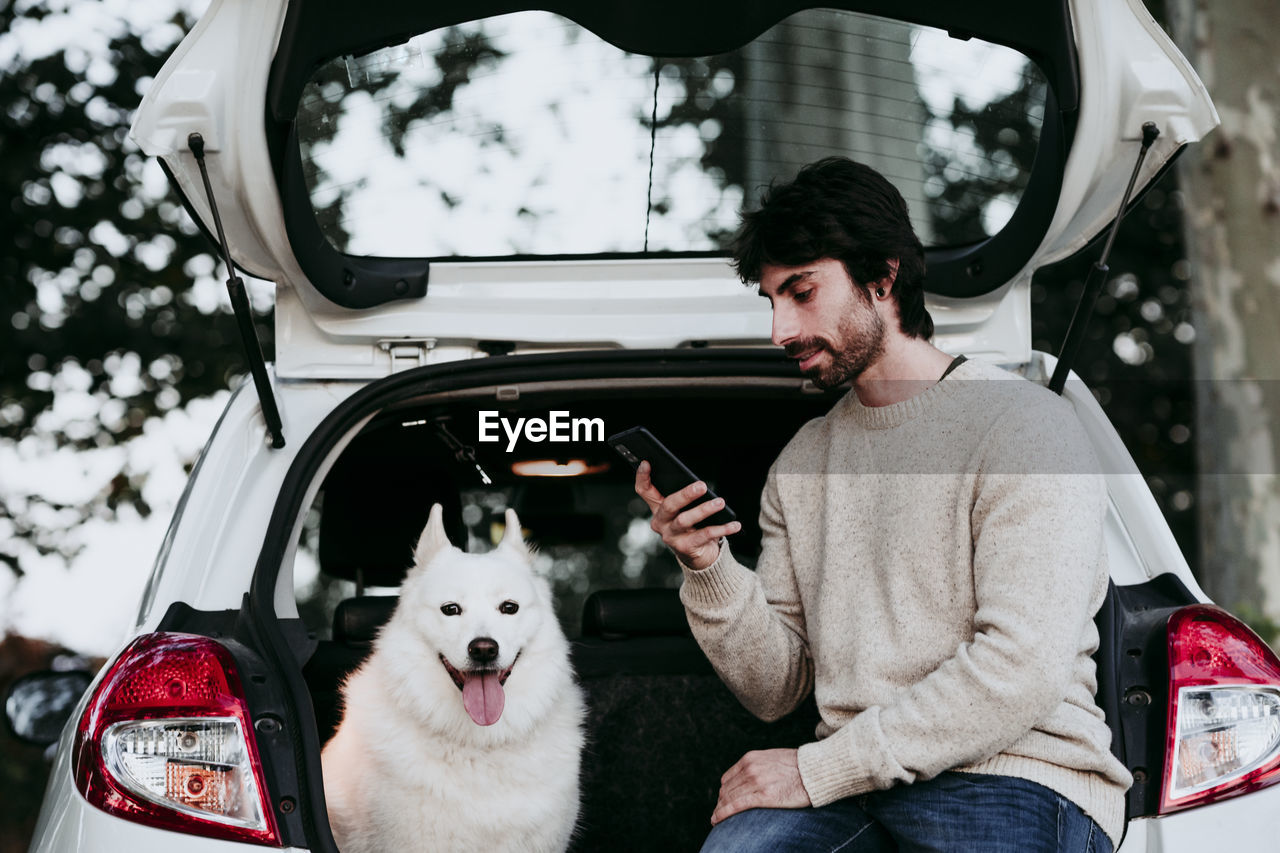 Mid adult man using mobile phone while sitting in car trunk at forest