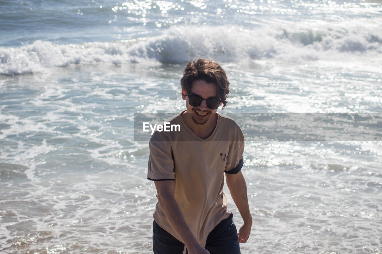 PORTRAIT OF SMILING YOUNG MAN STANDING AT BEACH