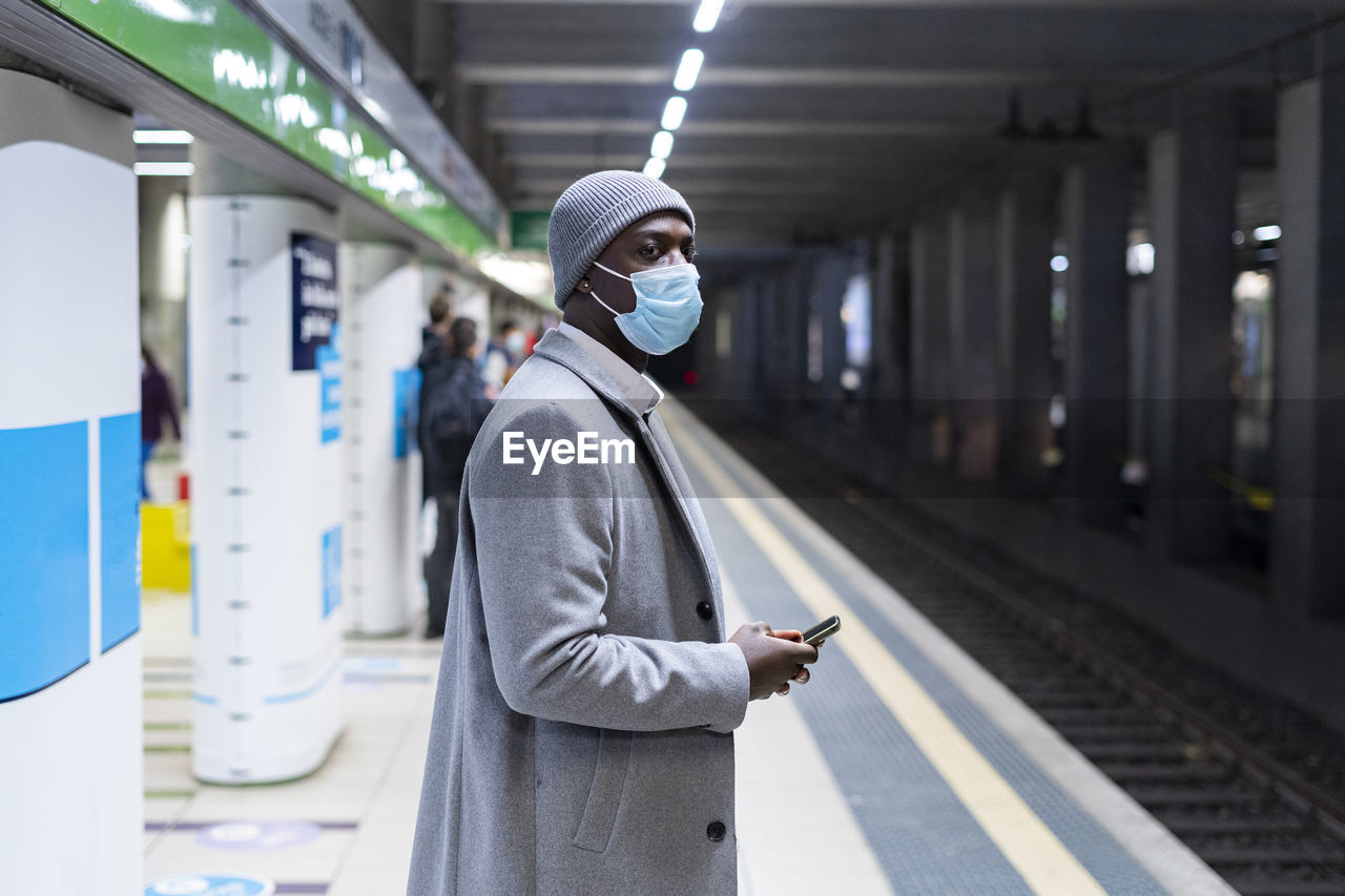 Thoughtful businessman with protective face mask standing at railroad station