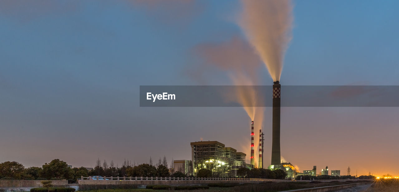 ILLUMINATED SMOKE EMITTING FROM FACTORY AGAINST SKY