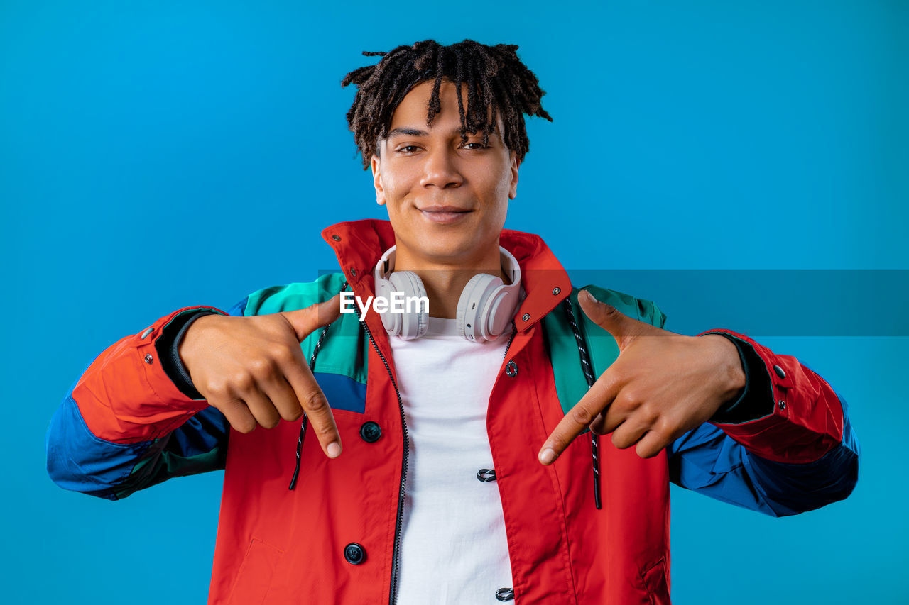 one person, colored background, portrait, blue, studio shot, clothing, sports, adult, young adult, blue background, waist up, front view, looking at camera, red, emotion, men, person, athlete, indoors, sports clothing, standing, smiling, lifestyles, vitality, happiness, black hair, exercising, copy space