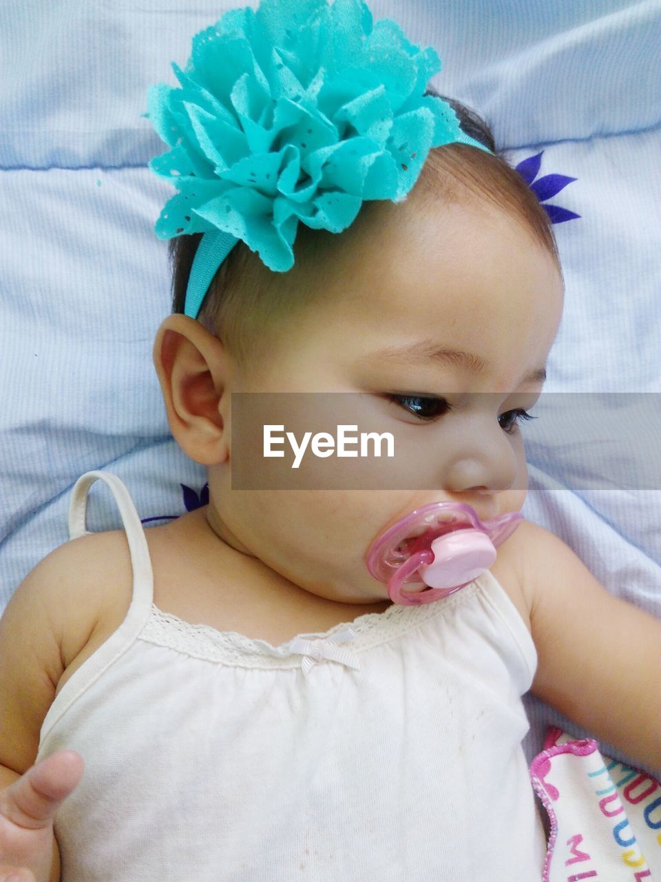 Close-up of cute baby with pacifier in mouth while lying on bed