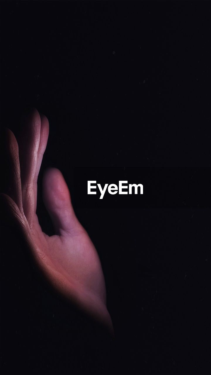 CLOSE-UP OF HUMAN HAND AGAINST BLACK BACKGROUND