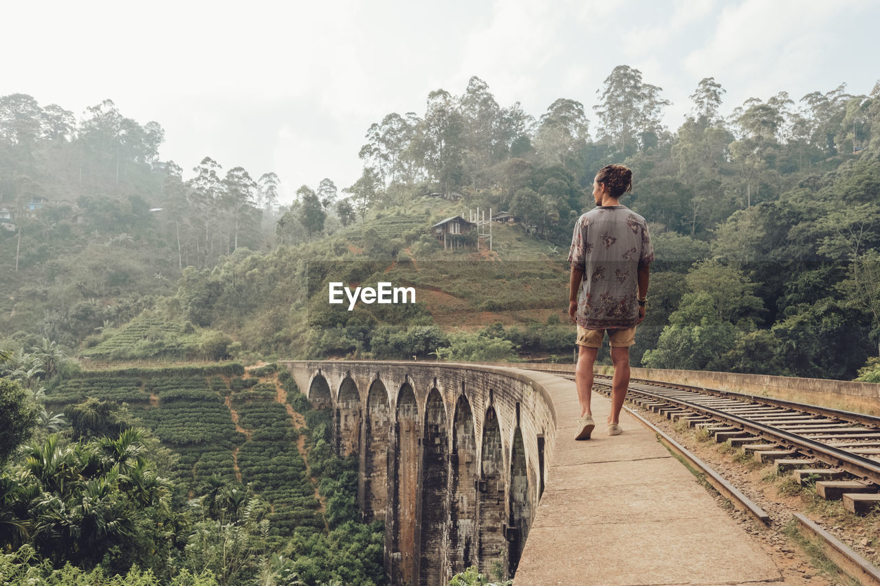 Male tourist walking on fence of bridge in tropical landscape in fog