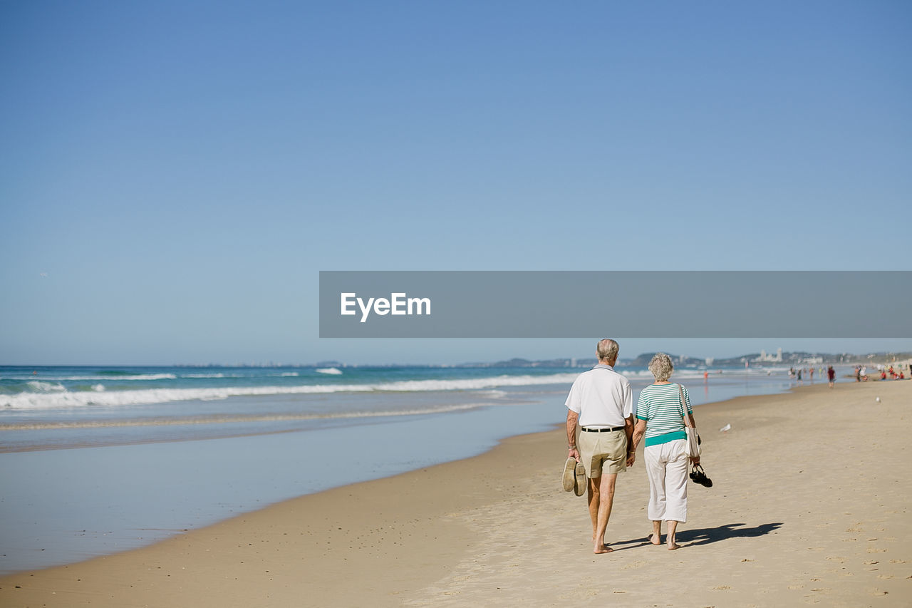 Rear view of man and woman walking at beach against clear sky