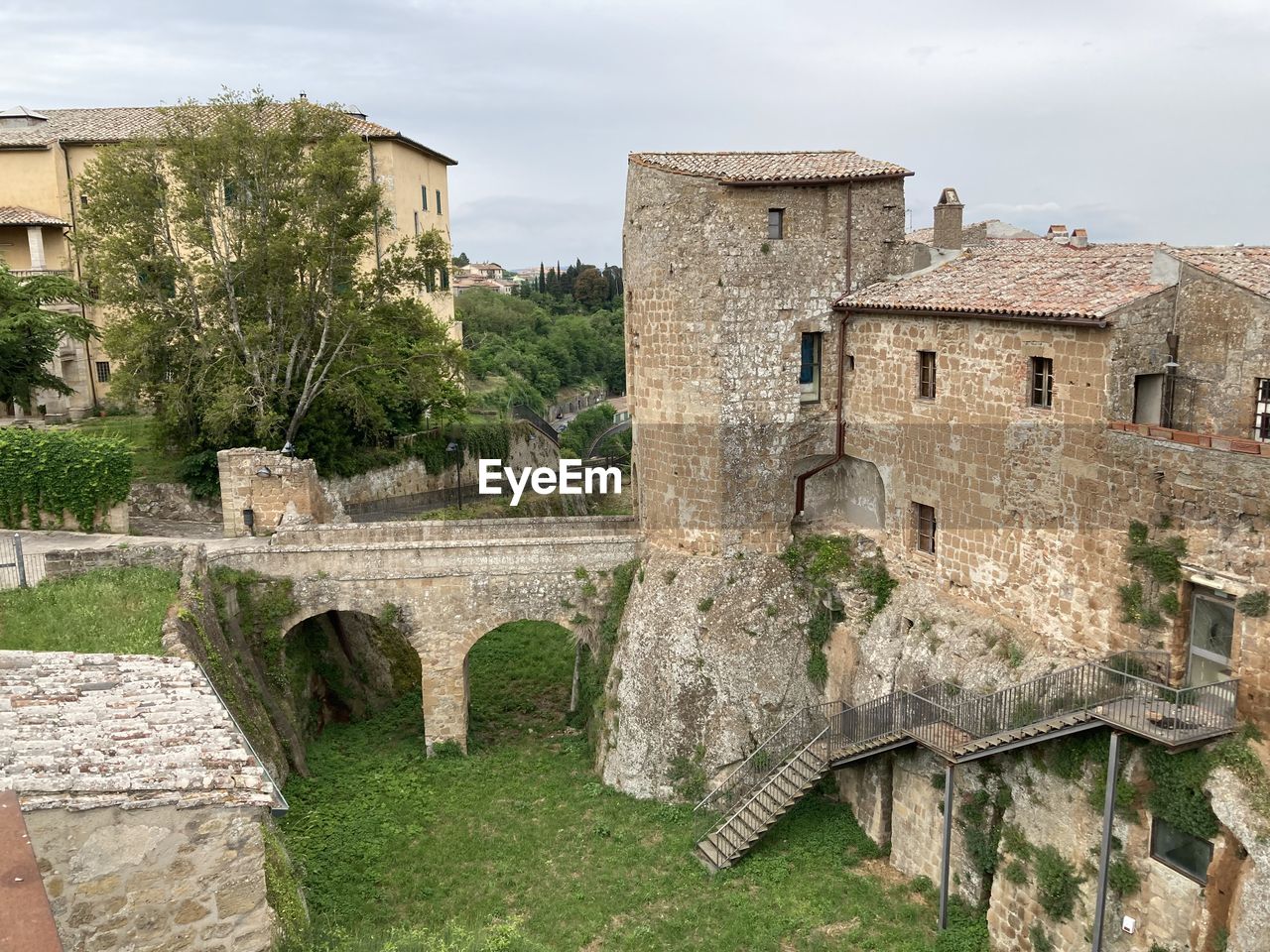 architecture, built structure, ruins, history, the past, building exterior, fortification, ancient history, building, old, village, castle, nature, plant, ancient, travel destinations, sky, wall, medieval, old ruin, no people, town, moat, tree, travel, house, stone material, château, fort, tourism, estate, cloud, residential district, outdoors, wall - building feature, stone wall, day, grass, landscape, historic site, land, city