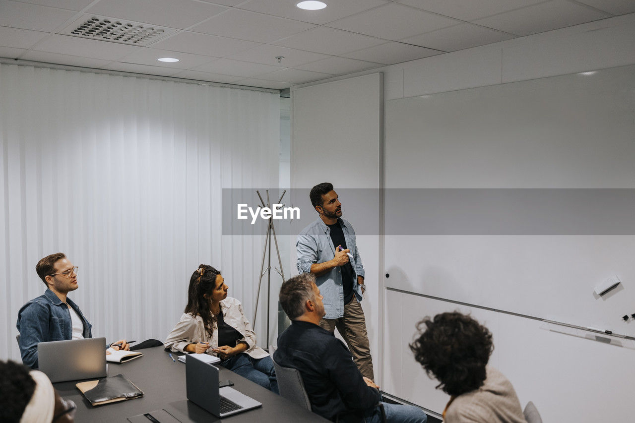 Mature businessman explaining strategy on whiteboard to colleagues in board room at office