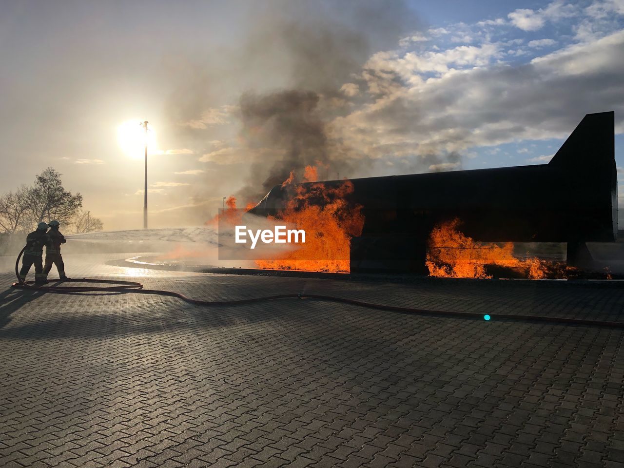 People on footpath by fire against sky in city