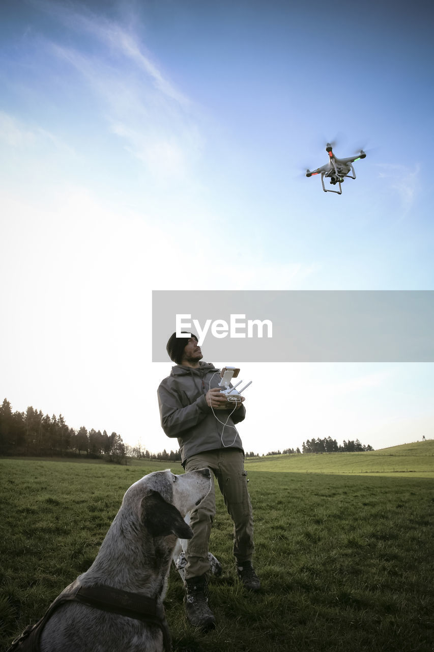 Man on a meadow flying drone while his dog watching